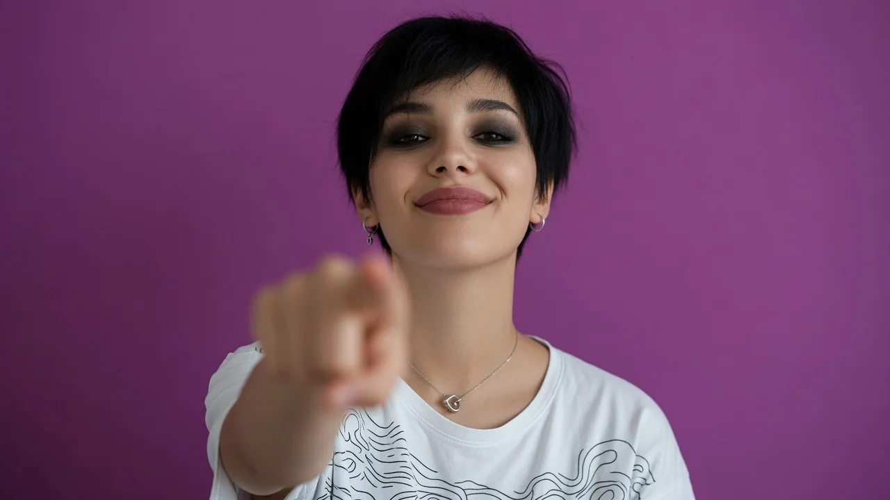 Smiling brunette with short hair pointing her finger toward the camera, pink background