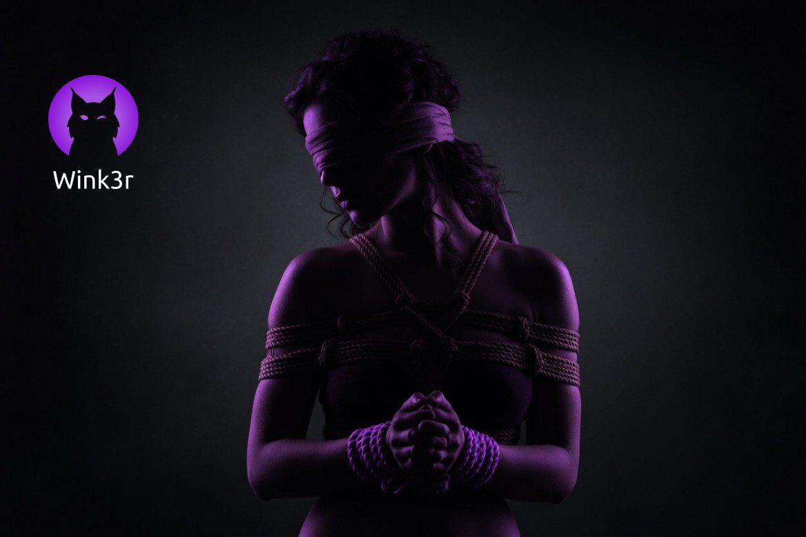A woman in a submissive role during a bondage session, blindfolded and wrapped in ropes around her shoulders and wrists, illuminated by purple light